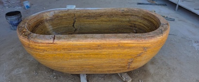 Natural travertine soaking tub with honey-beige veining and horizontal grain texture from Queretaro, Mexico.