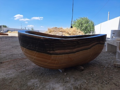Deep brown travertine stone soaking tub with charcoal and amber tones from Queretaro, Mexico